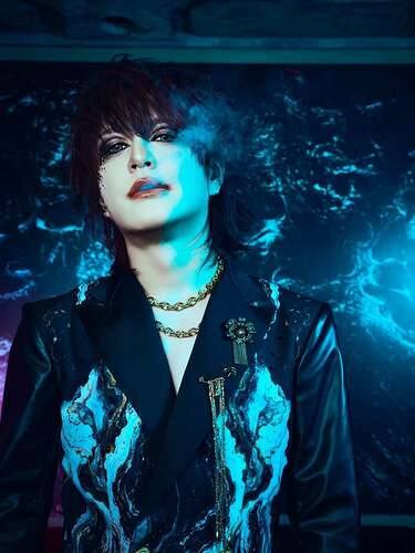 Dark shorter hair, black blazer with some white pattern, loosely reminding of smoke, two bigger golden necklaces, dark vibe eye make-up and lipstick, smoke coming from his mouth.